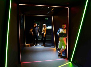 Three people standing in a dark space framed by lines of light