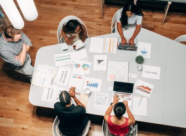 Birds eye view of group of people sat around a table with business strategy papers