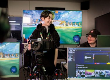 Esports students stood in front of digital screens with cameras