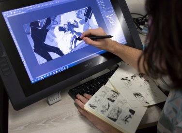 A hand holding a pen drawing game characters on a screen