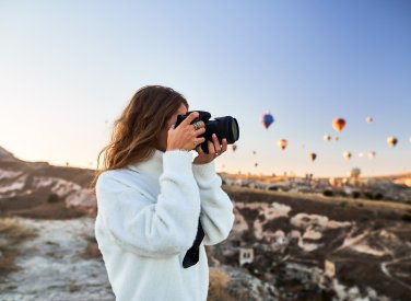 A student taking a photo standing underneath a sky full of hot air balloons