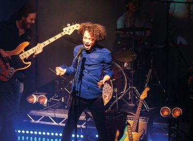 Student singing and jumping on stage in front of guitarist