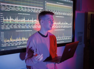 Student stood in front of large screen with code and graphs on