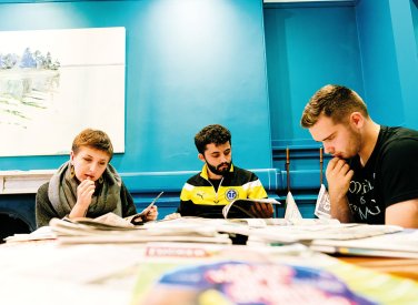 Students reading newspapers around a desk