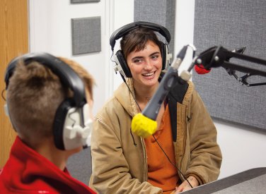 Students with headphones laughing and speaking into microphone