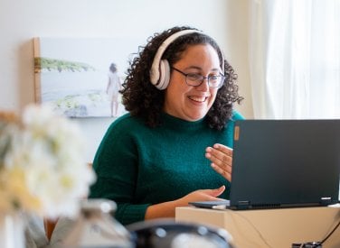 A woman wearing headphones smiling into her computer screen