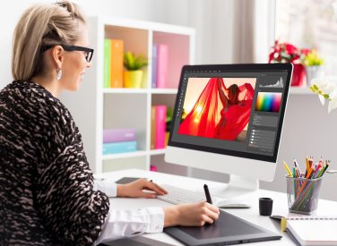A woman working on an iMac editing a photograph of a woman in a red shawl