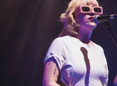 Blonde singer with sunglasses stood at microphone