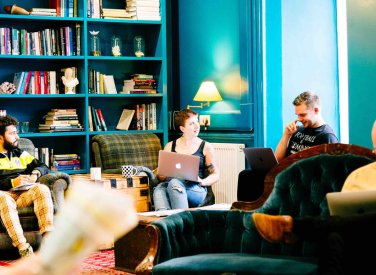 Falmouth University students sat on sofas in a blue room with bookshelves