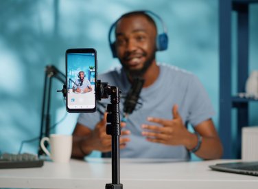 A man wearing headphones filming himself with his phone on a tripod