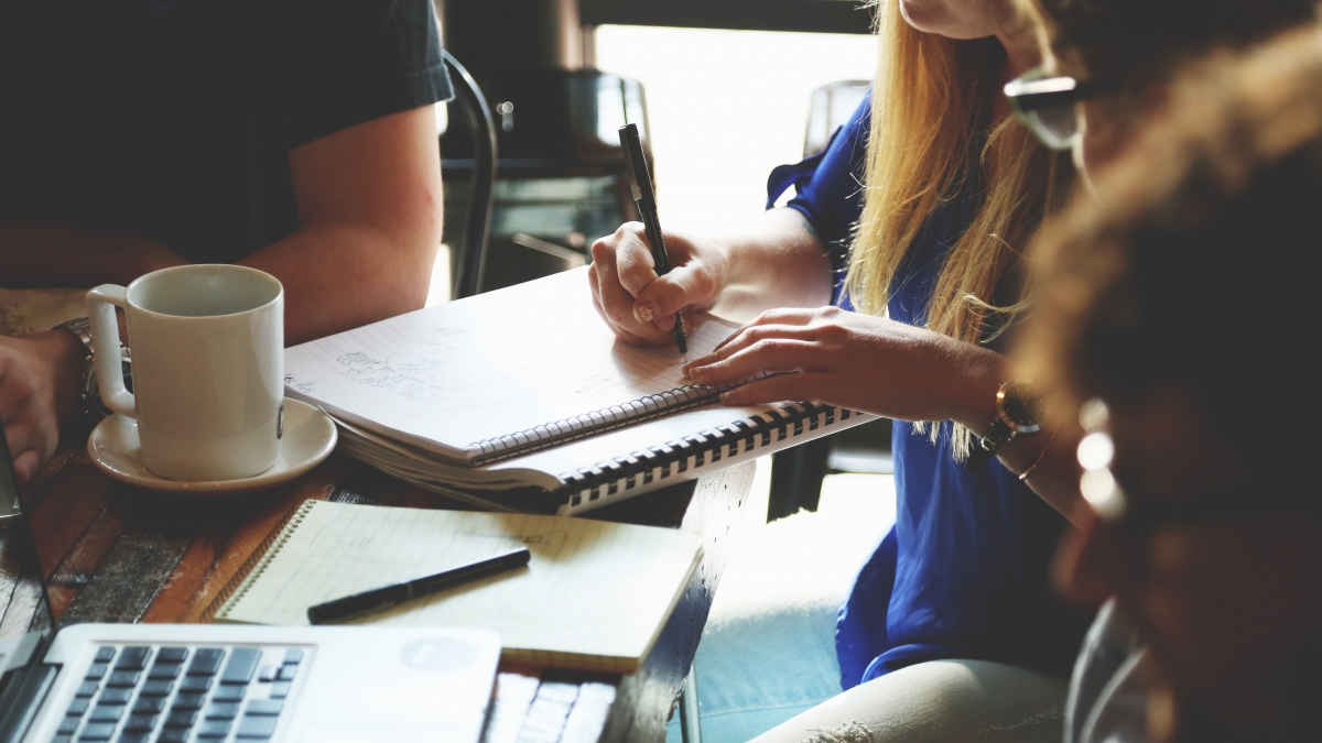 Business students sat around a desk, taking notes and drinking coffee.
