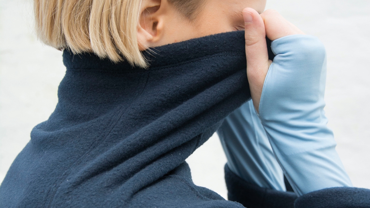 Model pulling dark blue fleece funnel neck up over face.