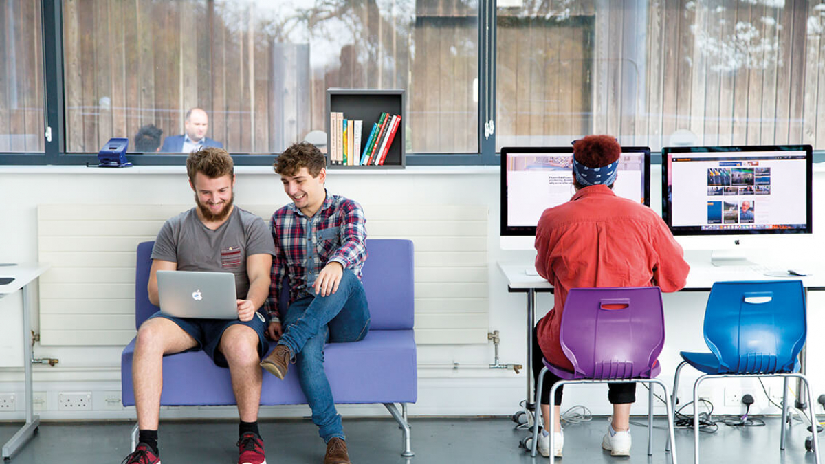 Three business management students working at a laptop and desktop
