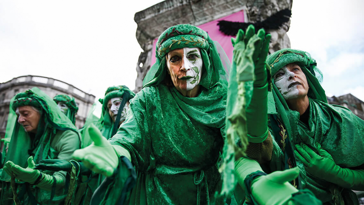 A group of people wearing green cloaks with white painted faces