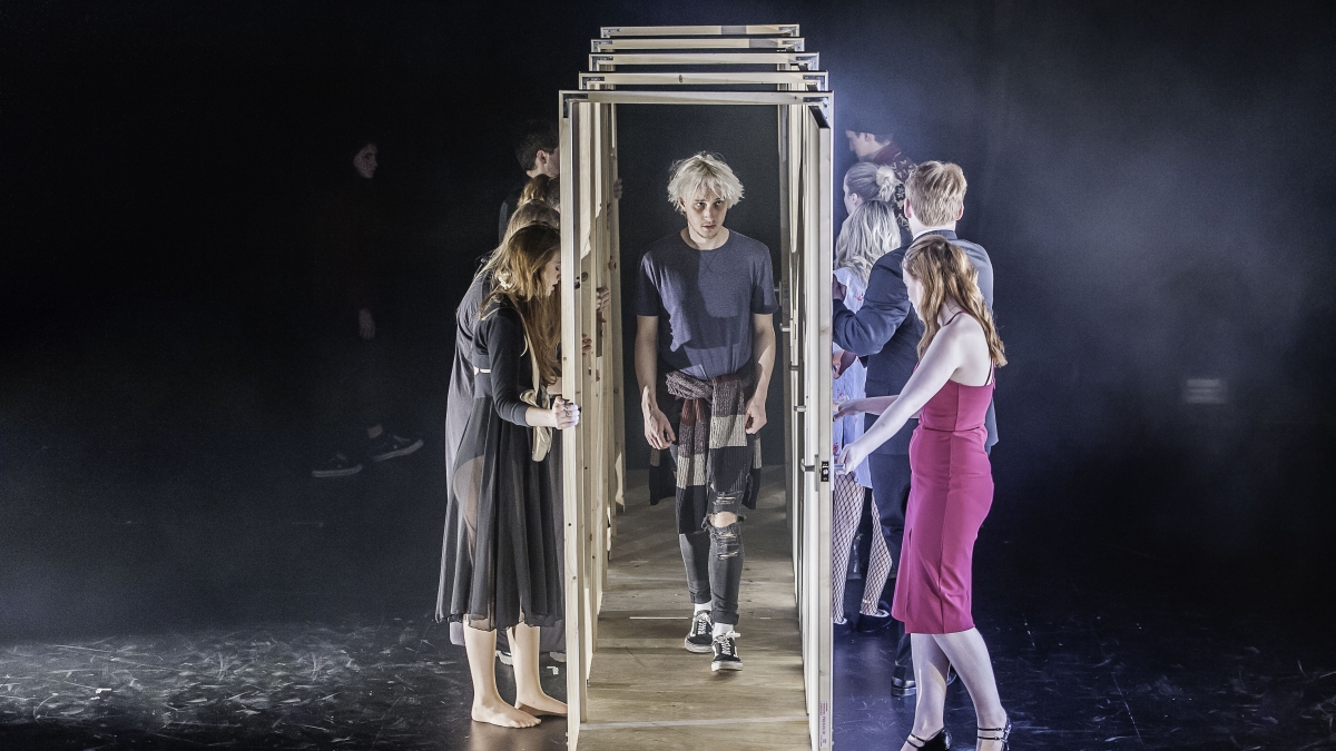 Actor walking through a series of open doors held by other members of the cast.