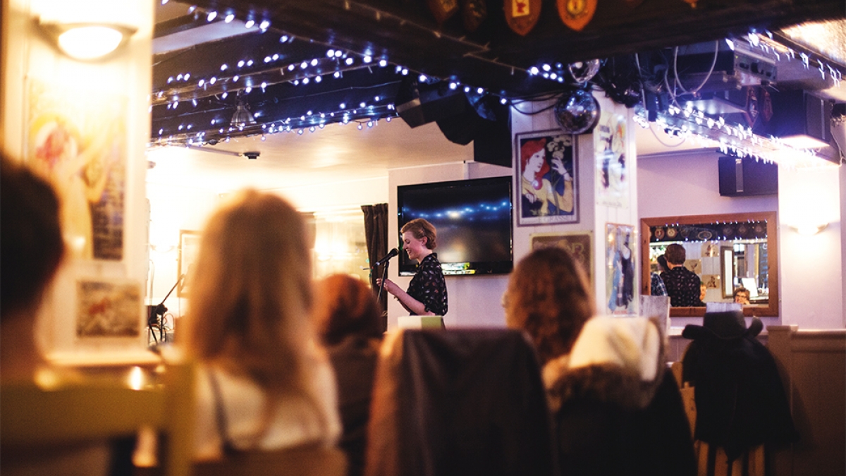 Student speaking into microphone at event in pub surrounded by blue fairy lights.