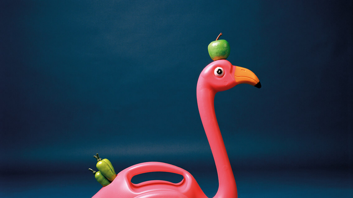 A pink plastic flamingo with a green apple on its head