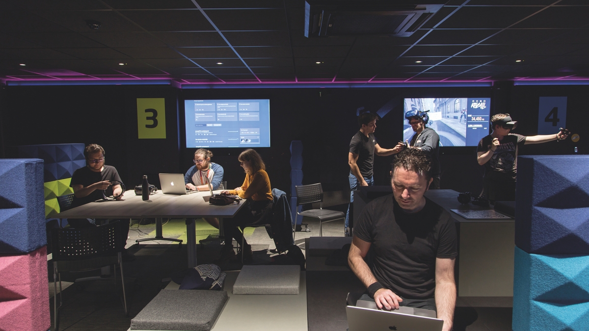 Students working on laptops in a game studio with screens