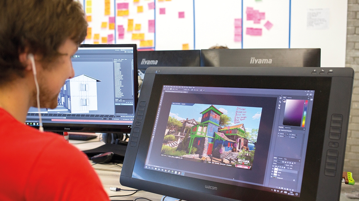 Games student with earphones and red t-shirt working at graphics tablet and creating an oriental building.