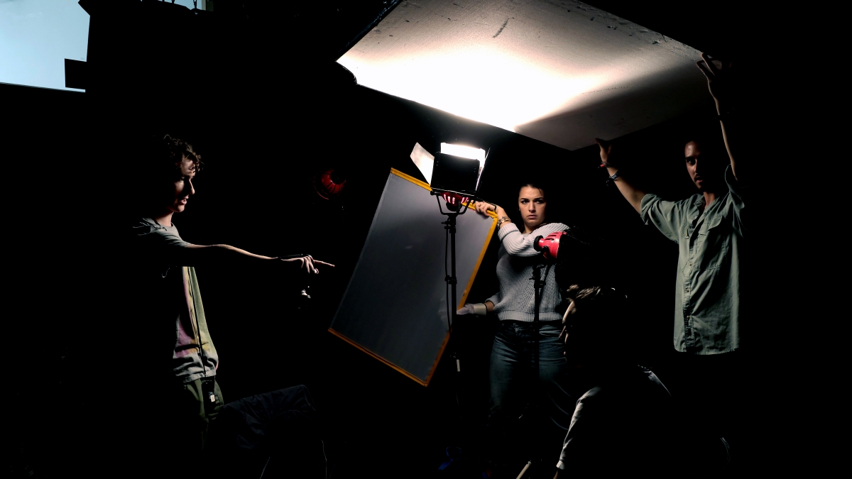 Falmouth film students holding up reflectors in dramatically lit studio.