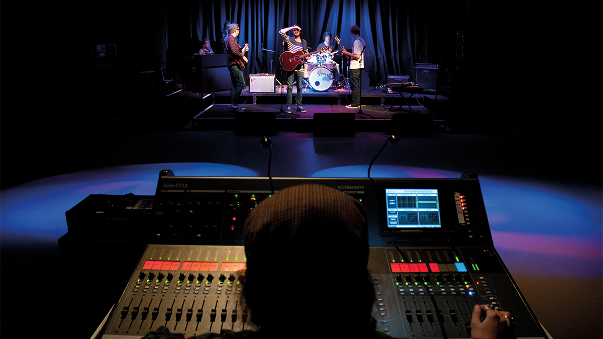 A person at a music desk while a band is on stage performing