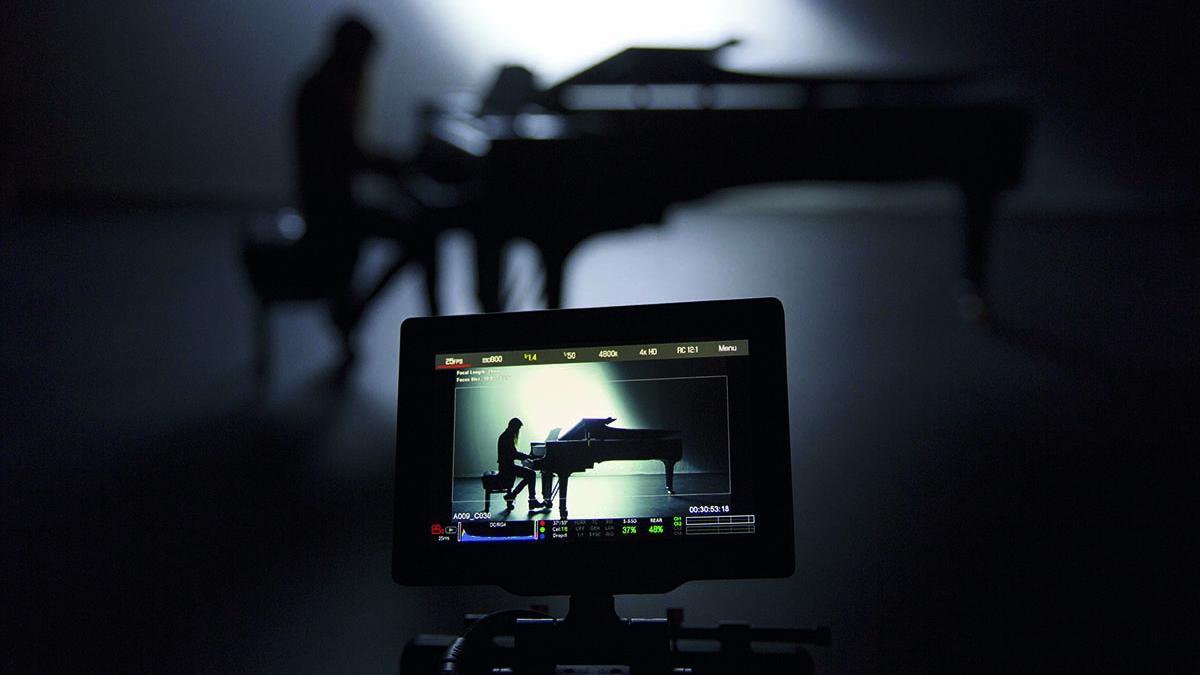 Student on a grand piano and the image on a camera viewfinder in the foreground.
