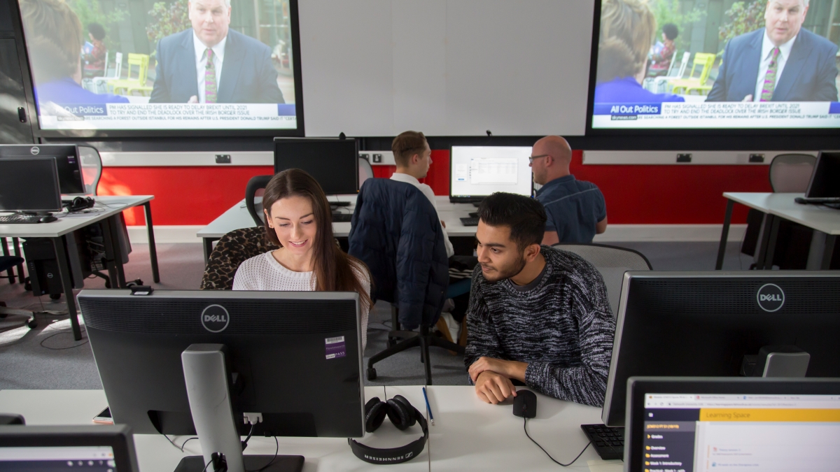 Students working together in newsroom, news playing on screens behind them.