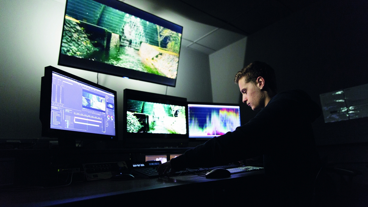 Student working in front of screens in editing suite.