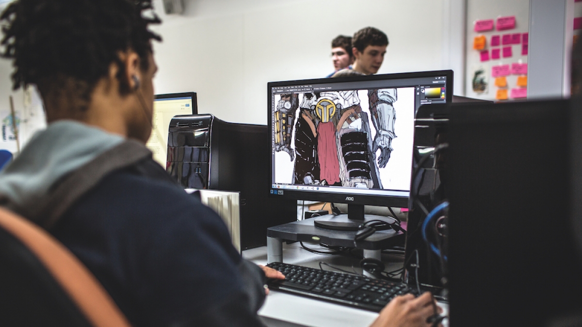 Game Art student working student seated at a desktop with game illustration on the screen