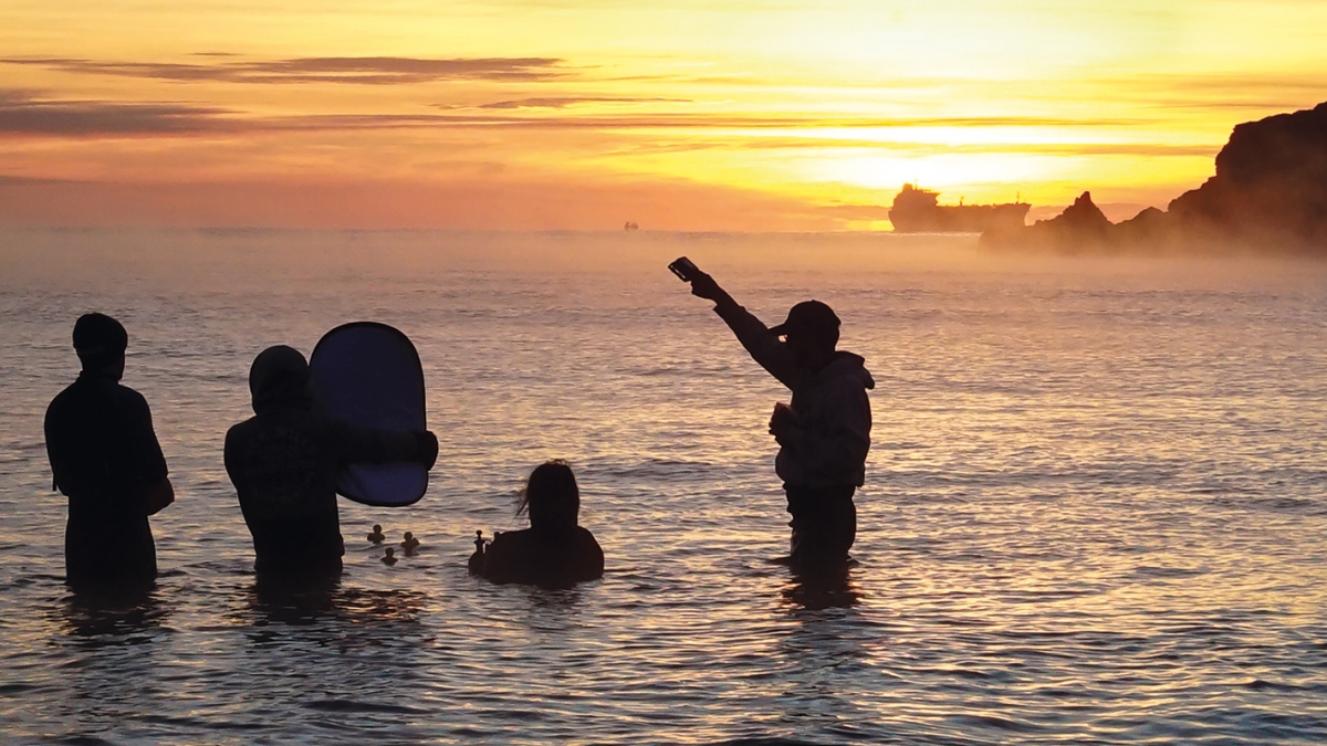Film students waist deep in sea filming rubber ducks.