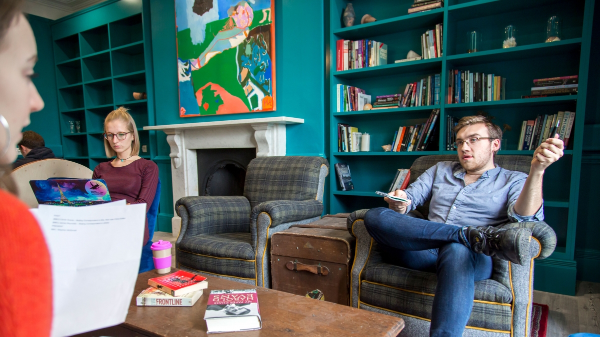 Students sitting in armchairs and discussing in the turquoise Writers' Room.