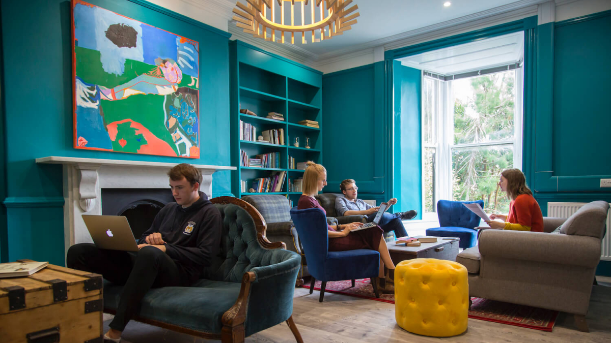 Falmouth University students sitting on armchairs and sofas in a teal room with wooden floor