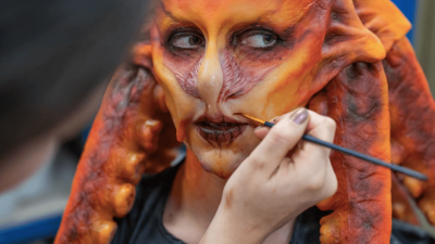 A person wearing a prosthetics orange mask with a hand and a paintbrush