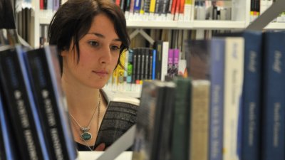 Student's face appearing through a gap in the books in the library.