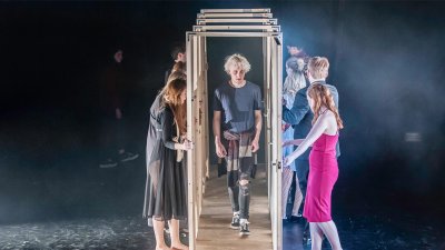 Actor walking through a series of open doors held by other members of the cast.