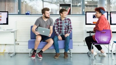 Students sat on seats with laptop on lap and discussing.