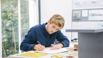 Falmouth University Architecture student working at a desk, wearing a blue shirt