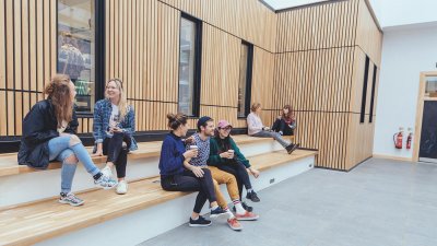 Falmouth University students sitting on steps with a wooden cladded wall behind