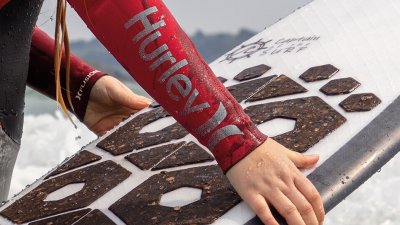 A person in a red Hurley wetsuit holding a surfboard