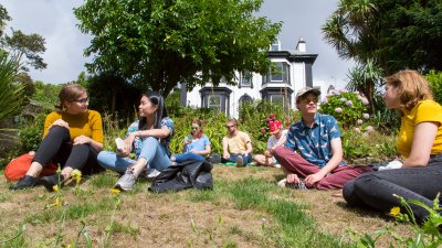 Students sat on the grass at Falmouth campus in front of an old black and shite Victorian building.