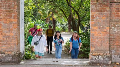 Students walking towards a gateway between red brick walls on Falmouth campus.