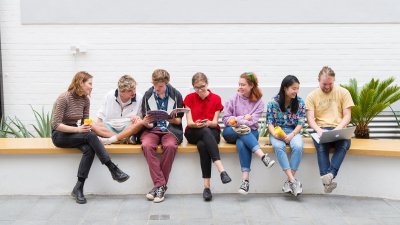 A group of Falmouth University students sitting on a wall inside a white building