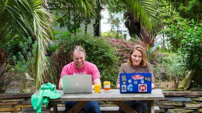 Students working at laptops below palm tree on Falmouth campus.