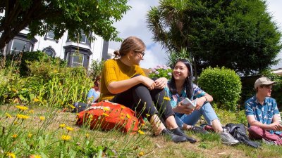 Falmouth University students sat and chatting in gardens on Falmouth Campus