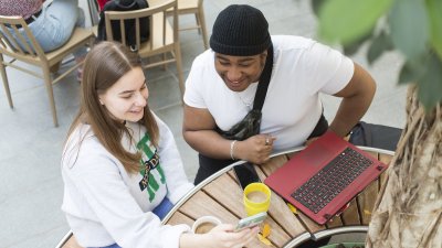 Two students sitting at a table with a laptop and drinks