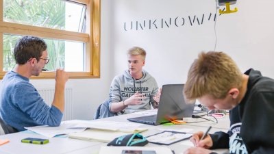 Three male students working at a large table with books