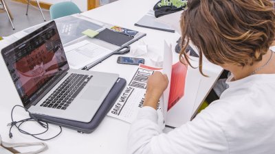 Graphic Design student at a laptop with papers