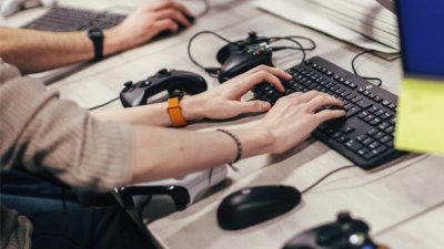 Hands typing on a keyboard with playstation controllers on the table