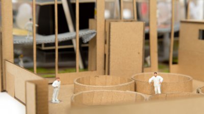 Cardboards mock up of interior with miniature figures of people in white suits.