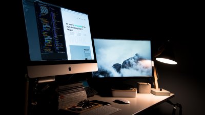 Desktop screens lit up in a dark room.